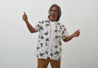 Naklejka premium Happy senior traveler asian man wearing glasses, summer shirt and brown shorts making thumbs up over white wall background, Business summer holiday concept