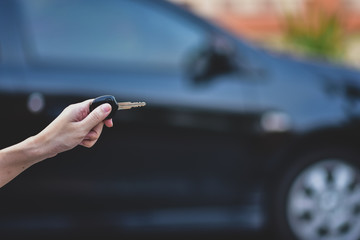 Hand holding Key and Car parked background