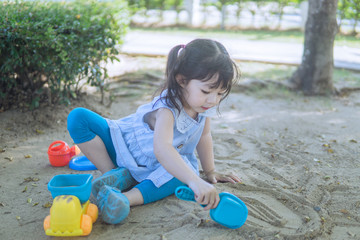 Cute Asian toddler girl playing in sand on outdoor playground.