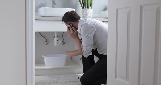 Man At Home Calling and Mopping Up Water From Leaking Pipe In Bathroom