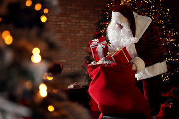 Santa Claus packing gifts into bag near Christmas tree