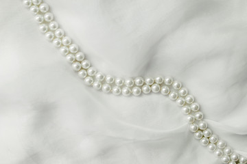 A necklace of pearls lies on a white cloth