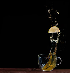 lemon flies into a Cup of tea with splashes on black background