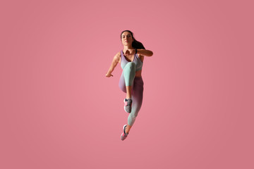Athletic young woman running on pink background