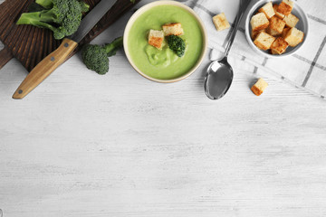 Delicious broccoli cream soup with croutons served on white wooden table, flat lay. Space for text