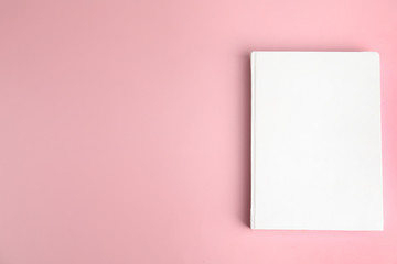 Book with blank cover on pink background, top view. Space for text