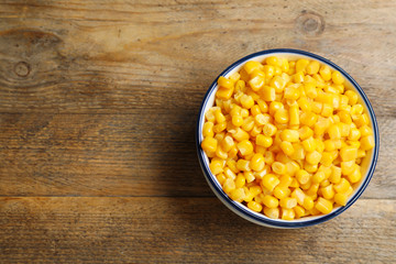 Delicious canned corn in bowl on wooden table, top view. Space for text