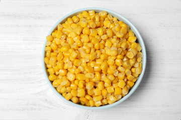 Delicious canned corn in bowl on white wooden table, top view