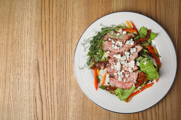 Delicious salad with roasted meat and vegetables served on wooden table, top view. Space for text