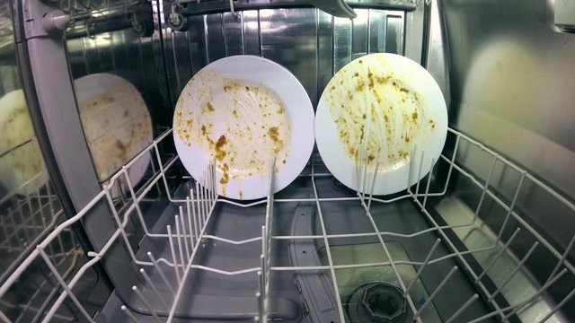 Inside the dishwasher. The process of washing dishes. Water jets spray and wash plates, mugs, forks, spoons and other utensils. The nozzle mechanism rotates. Digital camera inside the dishwasher.