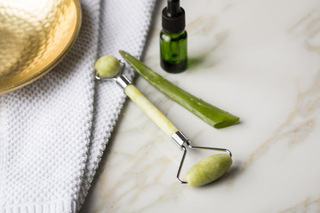 Massage Steinroller, Aloe Vera Blatt und Naturkosmetik Beauty Öl Serum Flasche grün an Handtuch, Gold Metall Schale und Marmor Hintergrund 