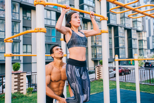 Fitness instructor helping woman on outdoor gym horizontal bar