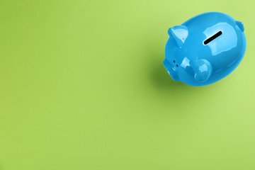 Blue piggy bank on green background, top view. Space for text