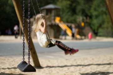 out of focus girl on a swing with playground in the background on a bright sunny day