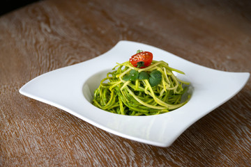 green spinach spaghetti with cheese and tomato on wooden table