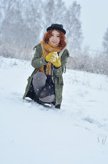 Fototapeta na wymiar Red-haired cheerful girl plays snowballs and enjoys the arrival of winterduring a snowfall