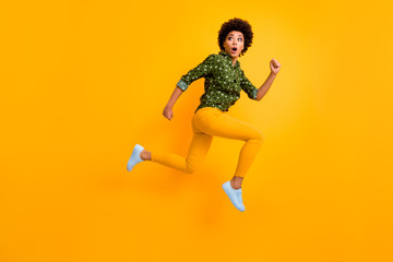 Fototapeta na wymiar Full body photo of crazy dark skin curly lady jumping up high rushing fast home see street dangerous maniac wear green dotted shirt pants sneakers isolated yellow color background