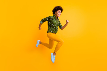 Full body photo of crazy dark skin curly lady jumping up high rushing fast discount shopping black friday prices wear green dotted shirt pants sneakers isolated yellow color background