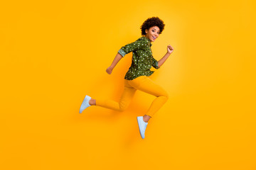 Fototapeta na wymiar Full size photo of crazy dark skin curly lady jumping up high rushing fast discount shopping black friday low prices wear green dotted shirt pants shoes isolated yellow color background