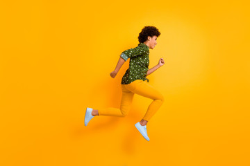 Fototapeta na wymiar Full length photo of funky dark skin curly lady jumping up high rushing fast discount shopping black friday low prices wear green dotted shirt trousers isolated yellow color background