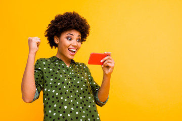 Portrait of surprised funky afro american girl use cellphone get win luck like notification scream wow omg raise fists wear stylish outfit isolated over bright color background