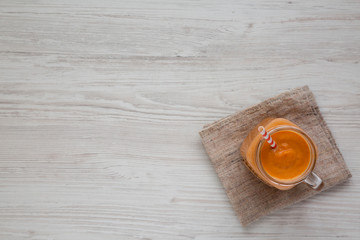 Homemade pumpkin smoothie in a glass jar on a white wooden surface. Flat lay, overhead, from above. Copy space.