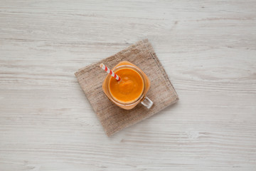 Homemade pumpkin smoothie in a glass jar on a white wooden surface. Flat lay, overhead, from above. Closeup.