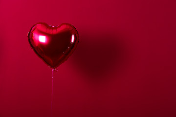 Celebrating Saint Valentine's Day with heart shaped red foil air balloon. Gift for loved woman on special occasion with romantic symbols, Women`s day. Close up, copy space, background, isolated.