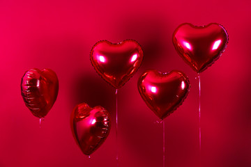 Celebrating Saint Valentine's Day with heart shaped red foil air balloon. Gift for loved woman on special occasion with romantic symbols, Women`s day. Close up, copy space, background, isolated.