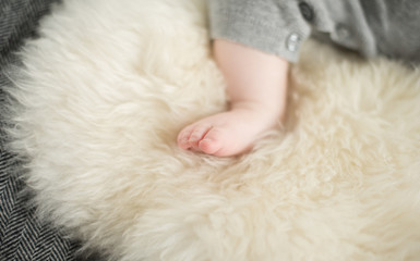 A beautiful soft delicate warm young baby foot photographed with a shallow depth of field. gentle calm colours and feel. baby care and well being. babies feet on a cream fur rug.