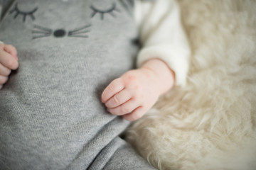 A beautiful soft delicate warm young baby hand photographed with a shallow depth of field. gentle calm colours and feel. baby care and well being. babies hands on a cream fur rug.