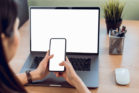 Woman hand holding smartphone with blank copy space screen for your advertisement. laptop on the table in office.