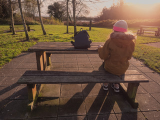 Young teenager girl sitting at wooden table in a town park. Warm sunny winter day, Sun flare.