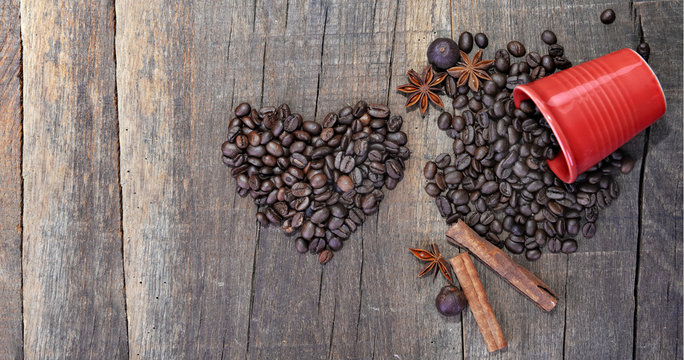 heart shaped with beans of coffee and red scattered red cup with spices on a rustic plank