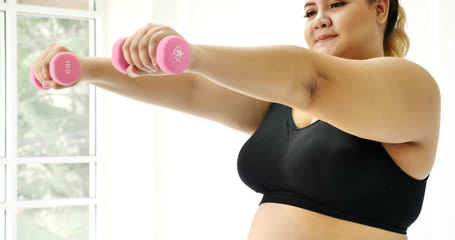 Chubby woman doing exercise by dumbbell in a room.