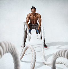 Muscular man working out with heavy ropes. Photo of handsome man with perfect body on grey...