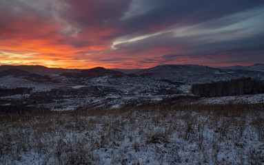 Winter dark sunset snow field on top of mountain slope on the background of  hills under colorful sky
