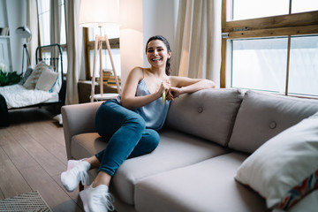 Laughing lady sitting on sofa with smartphone at home