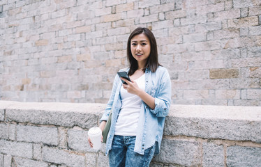 Modern Asian calm casual woman using smartphone on street