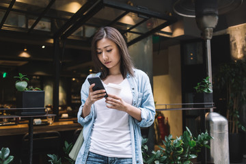 Young pretty woman surfing mobile while drinking takeaway coffee on street