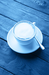 One cup of latte on a wooden background colored in blue trendy color