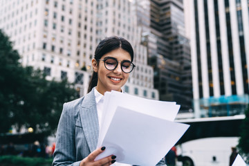 Successful businesswoman reading strategy information during accounting time at urban setting happy from good solutions, cheerful proud ceo in eyewear checking trade analyze for startup project