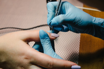 Fototapeta na wymiar Manicurist makes hardware manicure close-up. Treatment of nails with the help of hardware manicure