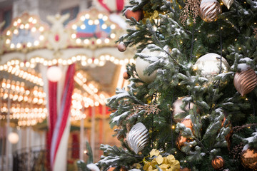 Big beautiful toys hang on a Christmas tree, hung with sparkling garlands and covered with snow. New Year decorations on the streets of Moscow. Christmas fir tree on the background of a carousel