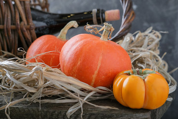 A new crop, two pumpkins and a ripe persimmon lie on a straw on a shelf in a shed.