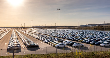New cars parked in a distribution center on a sunny day in the autumn, a car factory. Panorama of a...