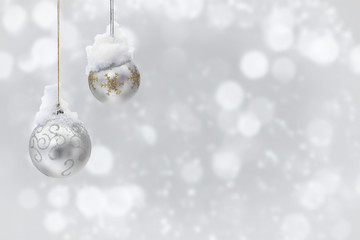 Hanging silver christmas balls covered snow on a blur light background with space for text