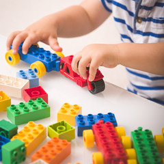 The boy plays colorful multi-colored cubes on the table. Early development and learning. Bright constructor for the game of plastic bricks.