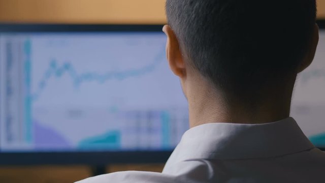 Businessman works at the computer, rear view. Male broker looks at stock sales statistics in the market.