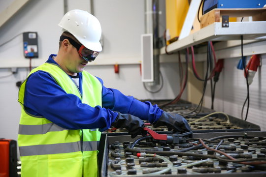 technician in a helmet and safety glasses includes charging batteries for forklifts in the battery room